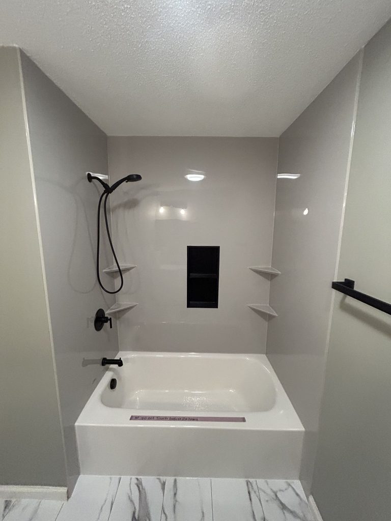 White Luxury Bath tub surround with matte black fixtures, recessed niche, and corner shelves