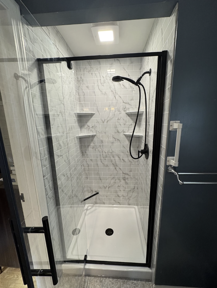 Luxury Bath walk-in shower installation with marble-pattern wall panels, black hardware, and built-in corner shelves