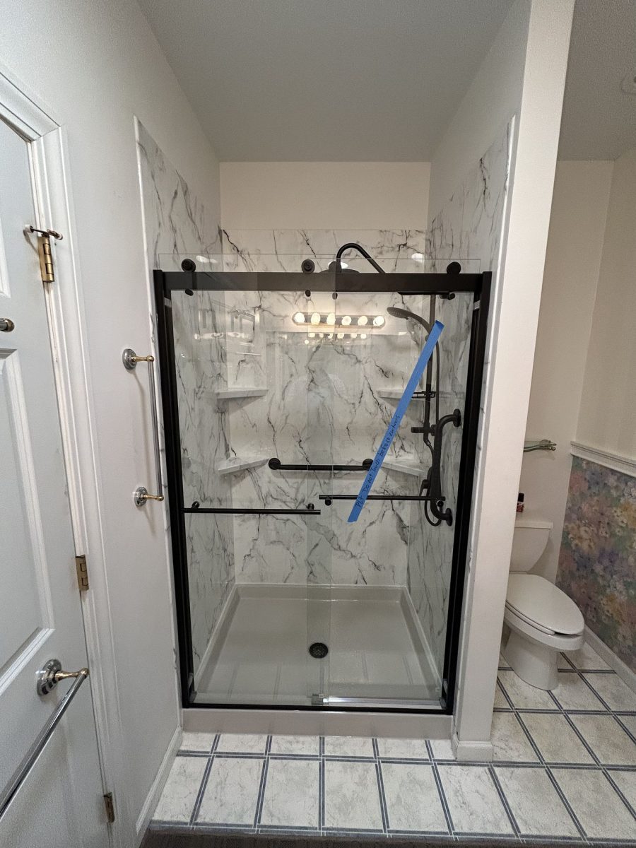 Completed bathroom remodel on Hawthorne Drive Berlin CT showing new Luxury Bath marble-look acrylic wall panels, matte black frameless sliding door, corner shelves, and rain shower head